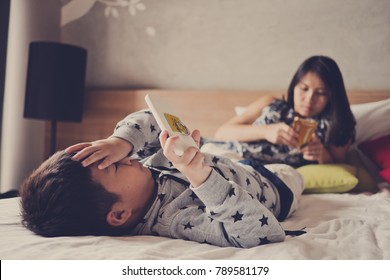 Asian  Chinese Children Playing Tablet With Mother On Bed . Boy Play Phone . Kid Playing Game . Child Use Smartphone
