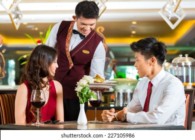 Asian Chinese couple - Man and woman - or lovers having a date or romantic dinner in a fancy restaurant while the waiter is serving food - Powered by Shutterstock