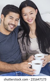 Asian Chinese Couple Relaxing At Home Drinking Mugs Or Cups Of Tea Or Coffee.