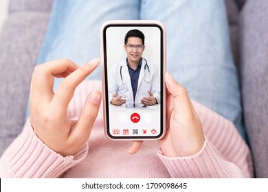 Asian chinese doctor or therapist help releave stress from coronavirus crisis video conference call online live talk remotely with woman sit on sofa couch at home using smartphone doctor consultation.