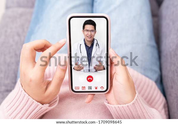 Asian chinese doctor or therapist help\
releave stress from coronavirus crisis video conference call online\
live talk remotely with woman sit on sofa couch at home using\
smartphone doctor\
consultation.