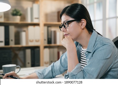 Asian Chinese Female College Student Work On Laptop Computer In Bright Home. Elegant Pensive Girl Looks Thoughtful Aside And Thinking New Plan For Homework. Young Woman Prepare For Test Indoors.