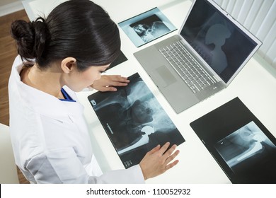 An Asian Chinese Female Medical Doctor Looking At X-rays Of Hip Replacement And Using Laptop In A Hospital