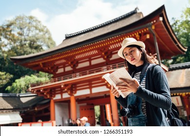 asian chinese female tourist with guide book in grand shrine. young girl reading kasuga taisha history information on sunny day while visiting sightseeing in nara japan. traditional old architecture. - Shutterstock ID 1266351193