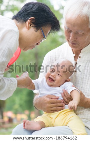Asian Chinese grandparents playing with baby grandson at outdoor garden.
