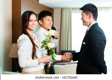 Asian Chinese Hotel Manager Or Director Or Supervisor Welcome Arriving VIP Guests With Roses On Arrival In Luxury Or Grand Hotel