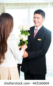 Asian Chinese Hotel Manager Or Director Or Supervisor Welcome Arriving VIP Guest With Roses On Arrival In Luxury Or Grand Hotel