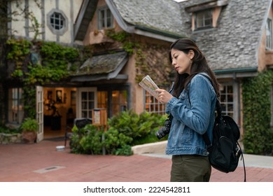 Asian Chinese Lady Solo Traveler Reading A Guide Map Near An Ivy Covered Cottage Style Hotel While Planning Her Route In Carmel By The Sea California Usa