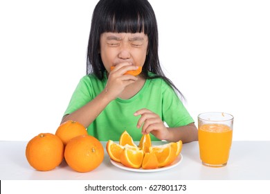 Asian Chinese Little Girl Eating Sour Orange And Making Grimace In Isolated White Background