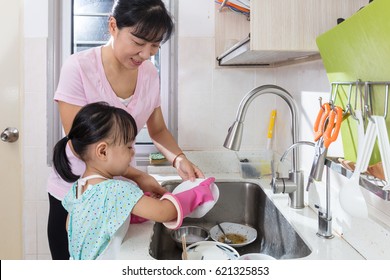 Asian Chinese little girl helping mother washing dishes in the kitchen at home