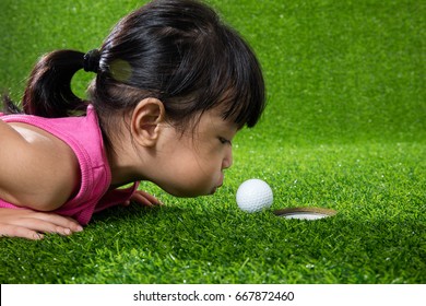 Asian Chinese little girl lying on grass and blowing the ball into a hole