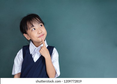 Asian Chinese little Girl thinking with finger on chin against green blackboard