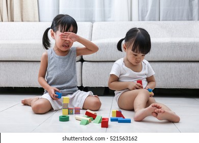 Asian Chinese little sisters struggle for blocks on the floor in the living room at home.
