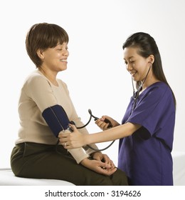 Asian Chinese Mid-adult Female Medical Practitioner Checking Blood Pressure Of African American Middle-aged Female Patient.