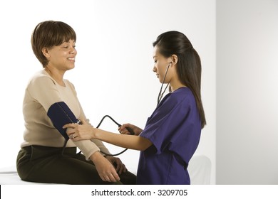 Asian Chinese Mid-adult Female Medical Practitioner Checking Blood Pressure Of African American Middle-aged Female Patient.