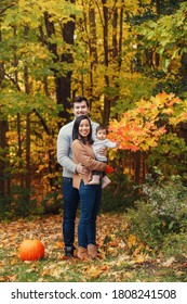 Asian Chinese Mother And Caucasian Father Dad With Baby Girl In Autumn Park Outdoor. Family Walking Posing In Fall Forest With Red Pumpkin. Halloween Or Thanksgiving Holiday.