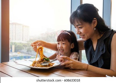 Asian Chinese mother and daughter eating spaghetti bolognese in the restaurant.