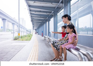 Asian Chinese mother and daughters waiting for a bus at bus stop