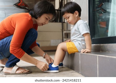 Asian Chinese mother helping her son put shoes on at home outdoors. First day of school. - Powered by Shutterstock