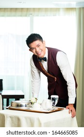 Asian Chinese room service waiter or steward serving guests food in a grand or luxury hotel room 