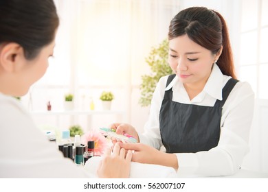 Asian Chinese Women Manicurist Showing Color Shellac Nail Polish At Nail Studio For Her Client To Chosing Color Of Nail Polish In Beauty Salon.