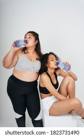 Asian Chubby And African Women In Sport Bra Drinking Water From Bottle At White Background.