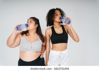 Asian Chubby And African Women In Sport Bra Drinking Water From Bottle At White Background.