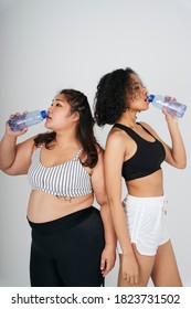 Asian Chubby And African Women In Sport Bra Drinking Water From Bottle At White Background.