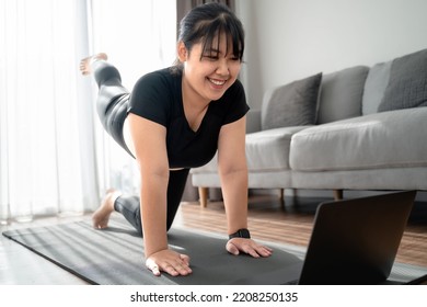 Asian Chubby Woman In Living Room Practice Online Yoga Lesson With The Computer. Female Having Meditate Training Class On The Laptop.