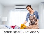 Asian cleaning service woman worker cleaning in living room at home. Beautiful young girl housekeeper cleaner feel tired and take messy dirty clothes into basket for housekeeping housework or chores.