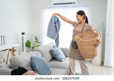 Asian Cleaning Service Woman Worker Cleaning In Living Room At Home. Beautiful Young Girl Housekeeper Cleaner Feel Happy And Take Messy Dirty Clothes Into Basket For Housekeeping Housework Or Chores.