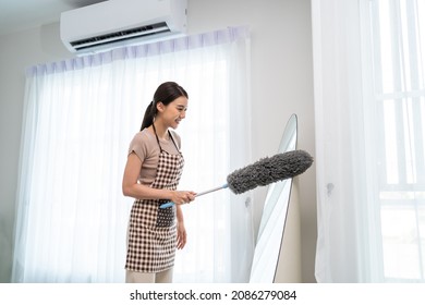Asian cleaning service woman worker cleaning in living room at home. Beautiful young girl housekeeper cleaner feel happy and use feather duster wiping messy dirty for housekeeping housework or chores