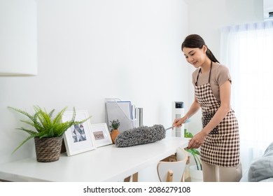 Asian Cleaning Service Woman Worker Cleaning In Living Room At Home. Beautiful Young Girl Housekeeper Cleaner Feel Happy And Use Feather Duster Wiping Messy Dirty For Housekeeping Housework Or Chores