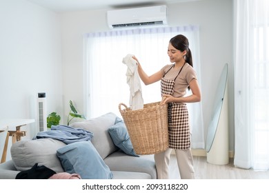 Asian Cleaning Service Woman Worker Cleaning In Living Room At Home. Beautiful Young Girl Housekeeper Cleaner Feel Happy And Take Messy Dirty Clothes Into Basket For Housekeeping Housework Or Chores.