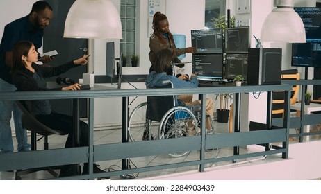 Asian coder with physical disability working with african american developer to create security firewall on terminasl window. IT engineer in wheelchair programming html script code.