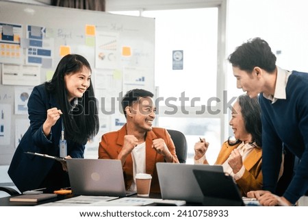 Asian colleagues are in a boardroom with laptops, enthusiastically engaging in a discussion, expressing happiness and satisfaction with their work.