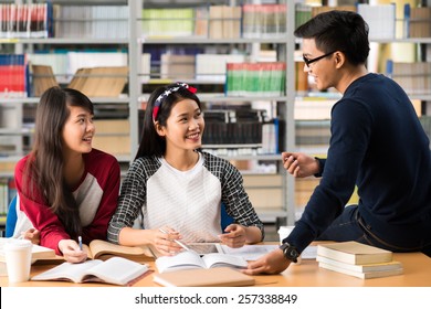 Asian College Students Talking While Doing Homework In The Library