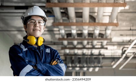 Asian confident man construction worker with protective suit, ear muffs, safety helmet and goggles standing with arms crossed looking at camera. Male maintenance engineer working at construction site - Powered by Shutterstock