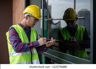 Asian construction worker or building inspector checking outdoor building construction structure or decoration detail by using check list.