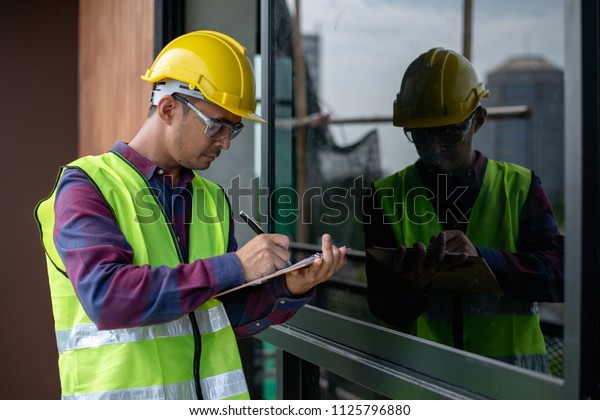 Asian construction worker or building inspector\
checking outdoor building construction structure or decoration\
detail by using check\
list.