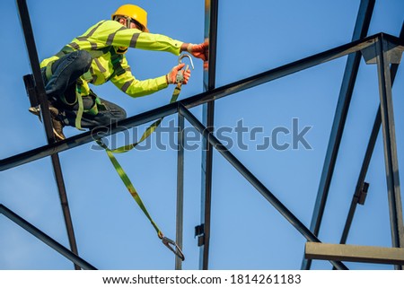 Asian construction worker Wear safety clothing and harnesses to do construction work on steel roof structures.