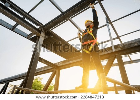 Asian construction worker wearing safety gear working at the construction site of the high roof structure of the factory.