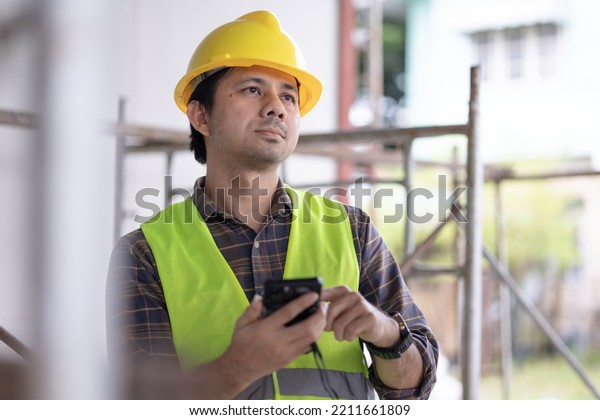 Asian construction workers use smart phones at\
construction site.