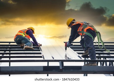 Asian construction workers wear safety straps while working on the roof structure of the building at a construction site. Roofer, using a pneumatic nail gun, install roof tiles.