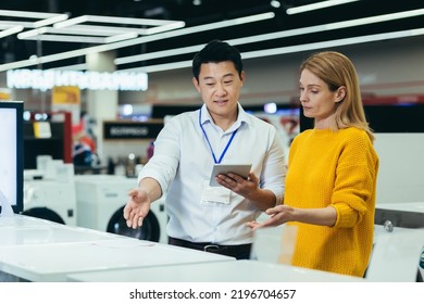Asian consultant salesman in electronics and household appliances store, selling a working machine to a woman, recommending and approving the choice