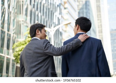 asian corporate executive giving subordinate a pat on the back while walking in street of central business district of modern city