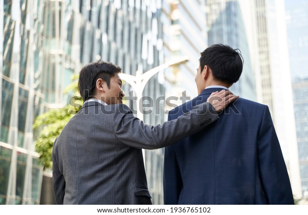asian corporate executive giving subordinate a pat\
on the back while walking in street of central business district of\
modern city