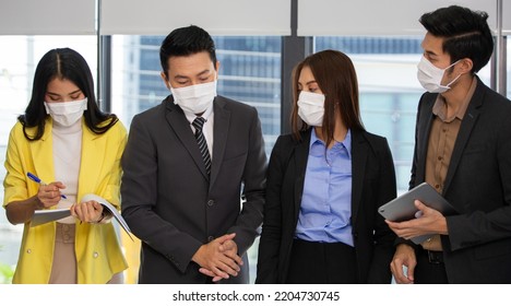 Asian Corporate Team Wearing Medical Face Mask Brainstorming, Discussing And Sharing Idea Of New Project At Office. New Normal Working And Social Distancing During Coronavirus Epidemic Concept