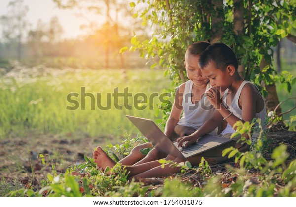 Asian country boys\
enjoying outdoors using laptop for self learning. Technology for\
education concept.