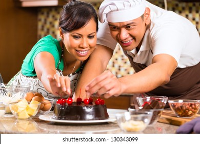 Asian Couple Baking Homemade Chocolate Cake With Cherries  In Their Kitchen For Dessert